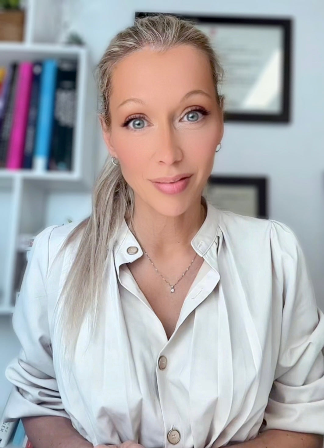 Portrait de Karine Sergerie, souriante, dans un environnement de bureau lumineux avec étagère et cadres en arrière-plan.
Portrait of Karine Sergerie, smiling, in a bright office environment with a shelf and frames in the background.